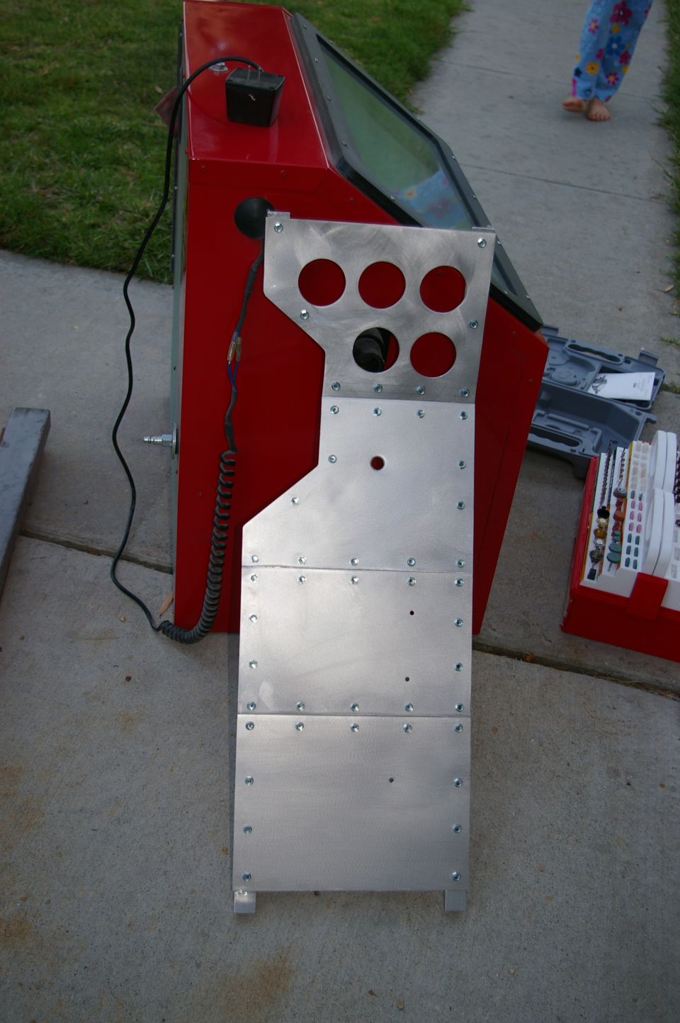 red sandblaster cabinet with a metal panel attached, showing six circular cutouts