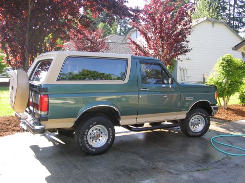 1990 Ford Bronco - Side view of a 1990 Ford Bronco parked in a driveway with trees and a house in the background.