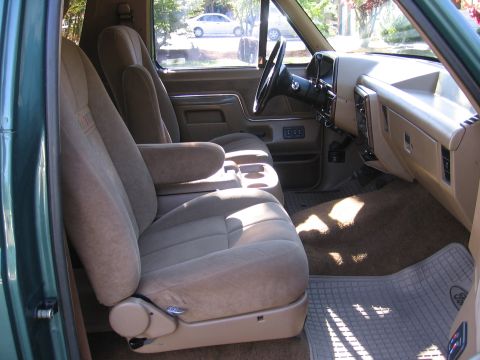 1990 Ford Bronco - The interior of a vehicle is shown, tan cloth seats and a beige dashboard with a black steering wheel.