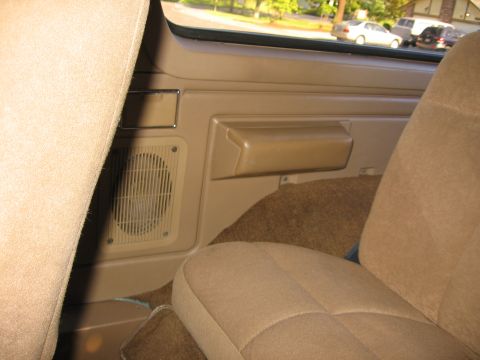 1990 Ford Bronco - Interior view of a tan door panel and seat, with a visible speaker grille and armrest.