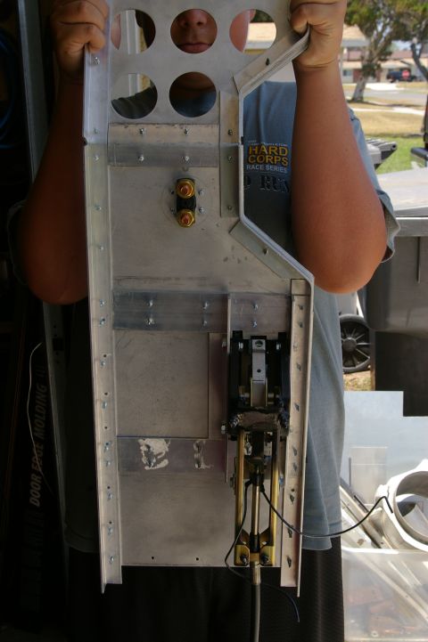 1986 Ford Bronco - Person holds a metal bracket assembly with mechanical components and circular holes.