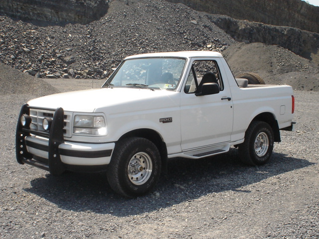 White 1995 Ford Bronco with a black bull bar on the front, parked on a gravel lot