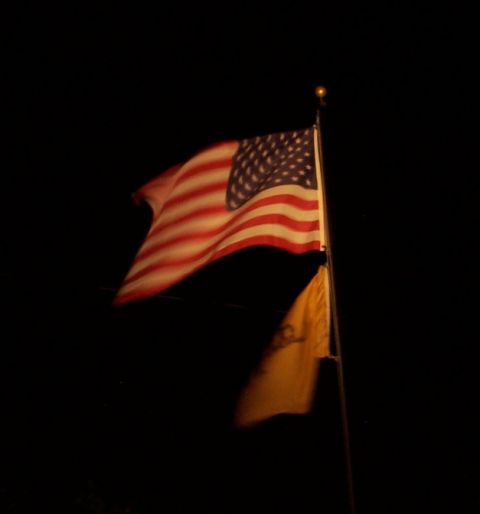 1990 Ford Bronco - Night shot of an illuminated American flag flying from a metal pole against a black sky, with a smaller yellow flag hanging below it. The g…