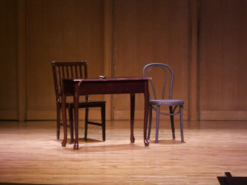 Stage set with a wooden table and two chairs on a wooden floor