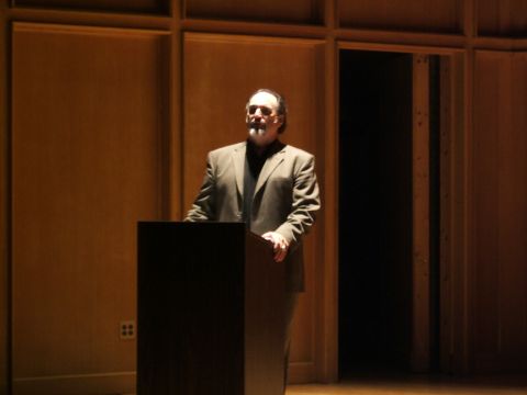 1996 Ford Probe - A man addresses an audience from behind a dark podium in a room with warm-toned wood paneling.