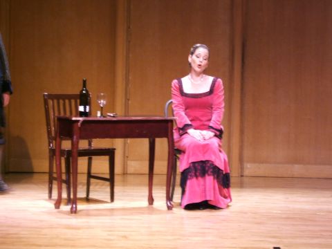 1996 Ford Probe - A woman in a pink gown performs on stage, seated at a table with a wine bottle and glass.
