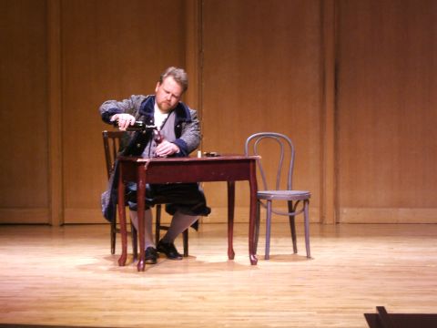 1996 Ford Probe - A man in period clothing is seated at a table on a stage, pouring wine from a bottle into a glass.