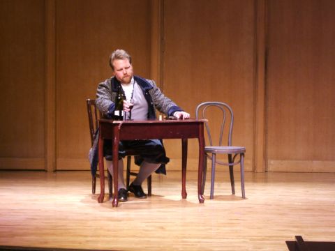 1996 Ford Probe - A man in period attire sits at a table on a stage, holding a wine bottle and glass.
