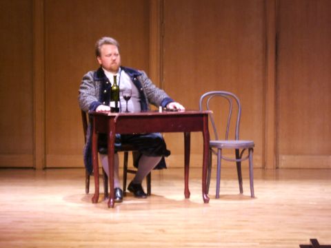 1996 Ford Probe - A man in period attire is seated at a table, with a bottle of wine and a glass before him on a stage.
