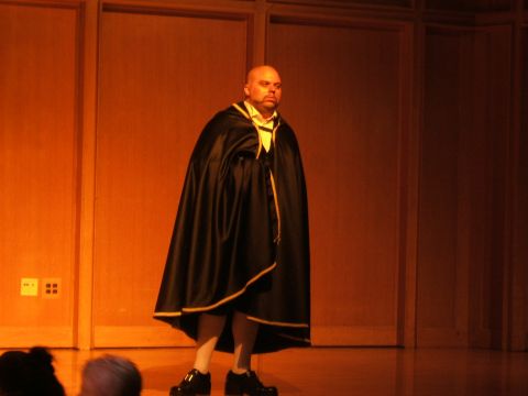 1996 Ford Probe - A man stands on a stage wearing a black cape over a white shirt and tie.