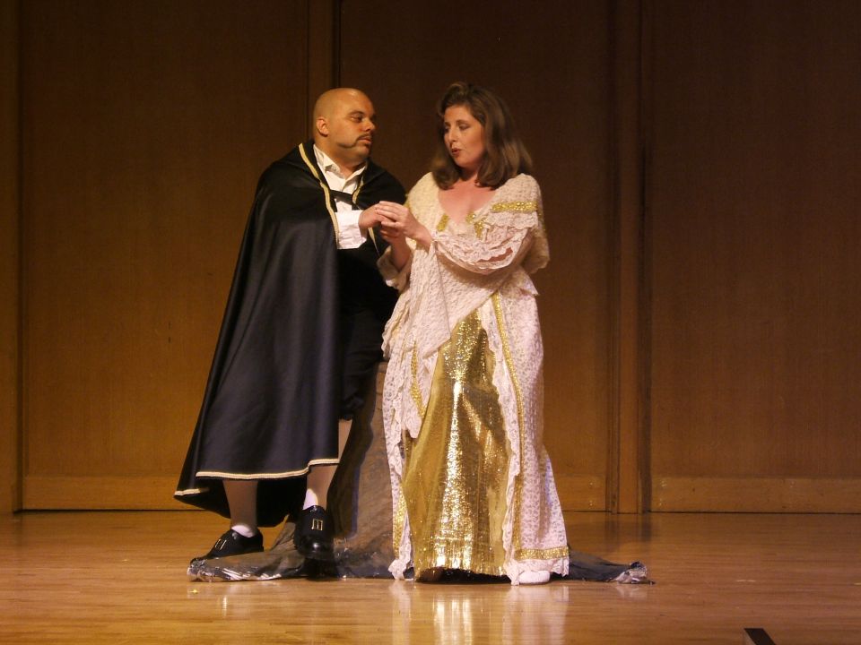 Man in cape and woman in ornate dress on stage
