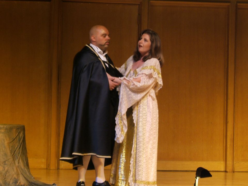 Stage actors in period costumes, a man in a black cape and a woman in a gold-patterned dress
