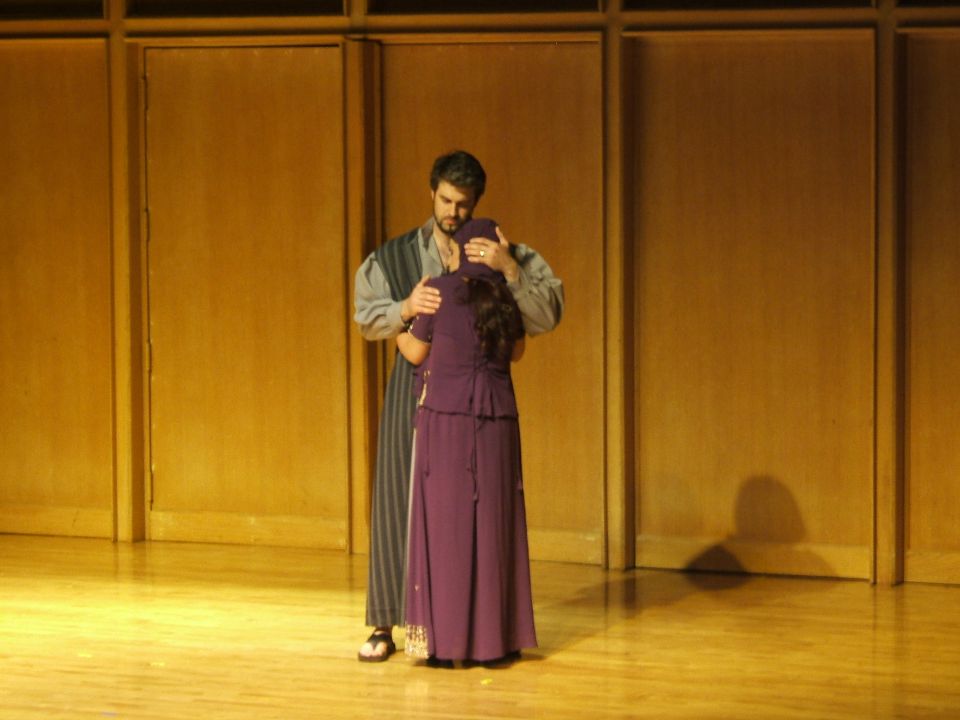 Man and woman in costume on stage, man embracing woman