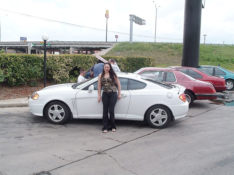 white coupe parked next to a woman, other cars behind it