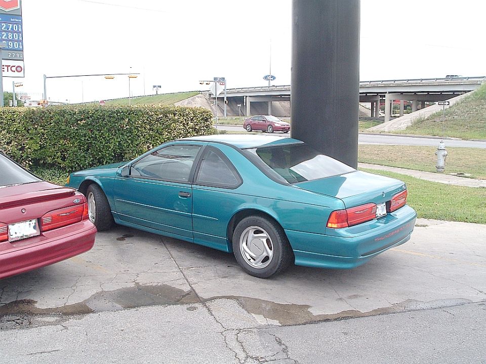 Teal Ford Thunderbird coupe rear three-quarter view parked at a gas station