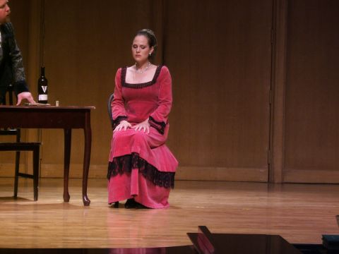 1996 Ford Probe - A woman in a period-style pink velvet dress with black lace trim is seated on a stage, with a table and chair to her left.