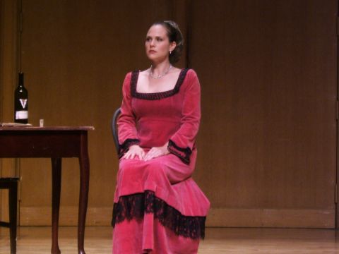 1996 Ford Probe - A woman in a period costume sits on a chair on a stage, with a table and wine bottle to her left.