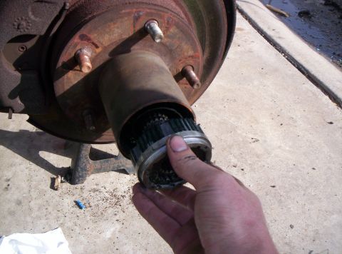 1986 Ford Bronco - A hand removes a manual locking hub from a vehicle's front wheel assembly, revealing gears and grease.