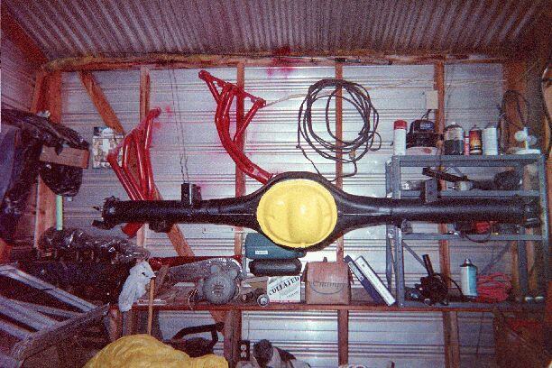 Black rear axle housing with yellow diff cover mounted on garage wall, red headers hanging above