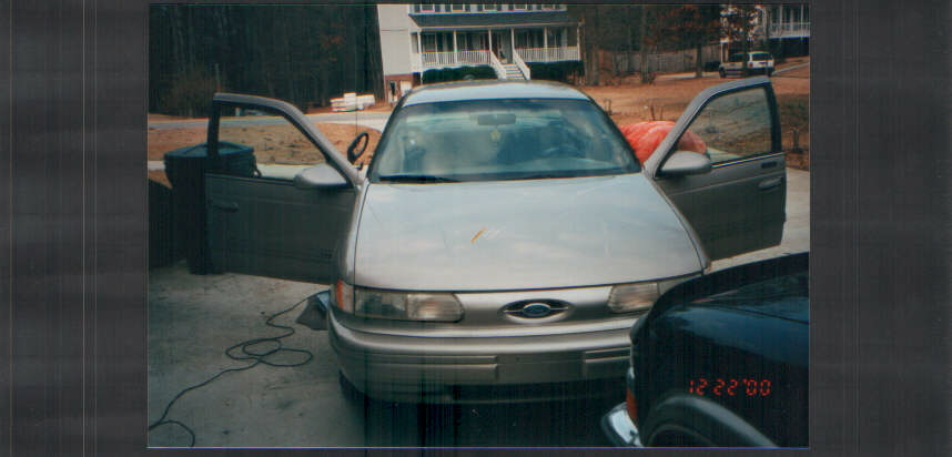 Front view of silver Ford Taurus sedan with both front doors open on a driveway, dated 12/22/00