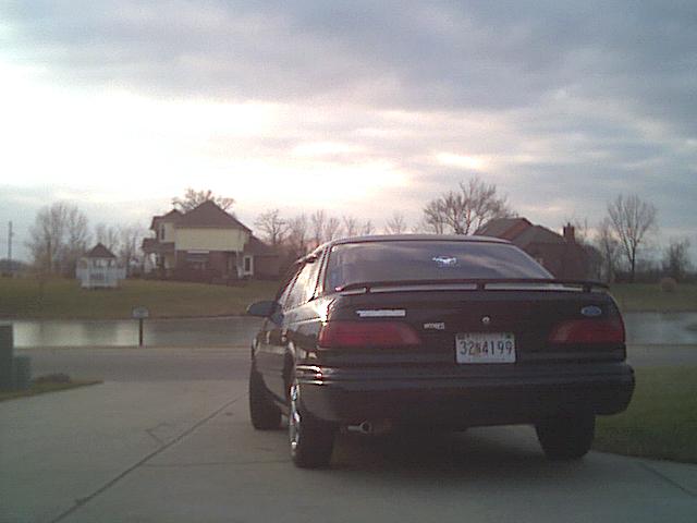 Dark Ford sedan rear view parked on driveway with spoiler and license plate under cloudy sky