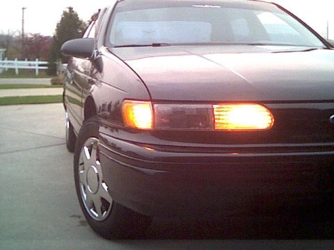 1993 Ford Taurus - The front passenger side of a dark sedan is shown with the turn signal illuminated.