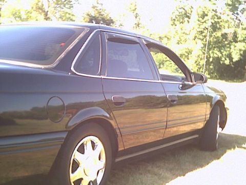 1993 Ford Taurus - Side profile of a dark 1993 Ford Taurus sedan parked outdoors.