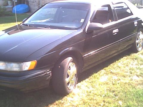 1993 Ford Taurus - A dark-colored sedan is parked outdoors on a grassy area, with a brick building in the background.