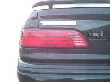 1993 Ford Taurus - The rear of a dark-colored sedan is shown, focusing on the taillight and a 'midnight' emblem.