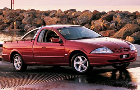 1993 Ford Taurus - This red ute, possibly a 1998 model, is parked near a rocky shoreline.