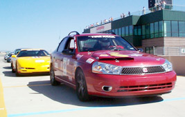 1993 Ford Taurus - A red sedan leads a yellow sports car on a sunny day at a race track.