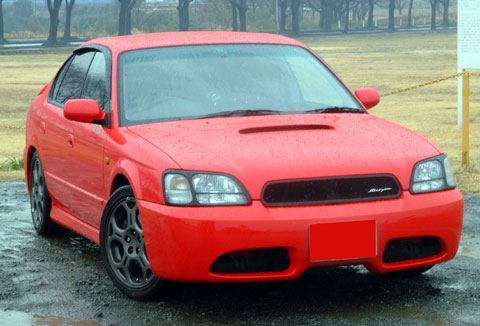 1993 Ford Taurus - A red Subaru Legacy sedan is shown from a three-quarter front view on a wet, overcast day.