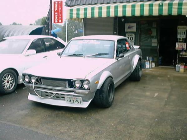 Silver 1970s Japanese coupe with flared fenders parked outside auto shop