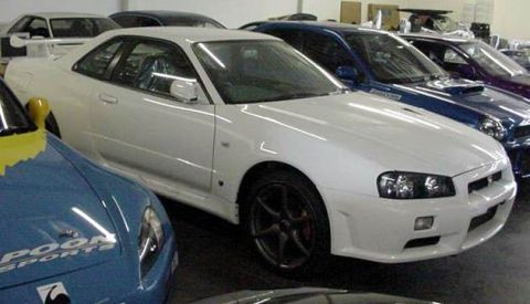 1993 Ford Taurus - A white coupe, likely a Nissan Skyline GT-R R34, is parked in a showroom with other vehicles.