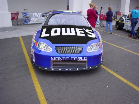 1993 Ford Taurus - A blue and black Lowe's race car with 'Monte Carlo' text on the front is parked in a lot, with other vehicles and people in the background.
