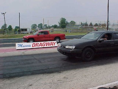 1993 Ford Taurus - A black 1993 Ford Taurus is lined up at the drag strip next to a red pickup truck.