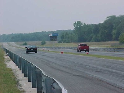 1993 Ford Taurus - Two vehicles compete on a drag racing track under an overcast sky.