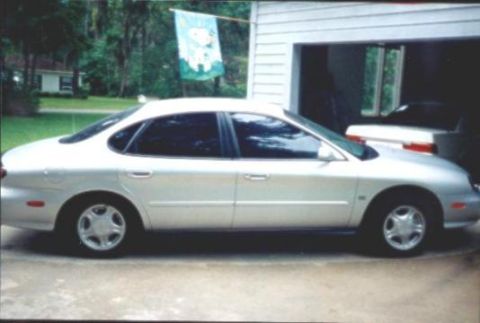1998 Ford Taurus - Side profile of a silver 1998 Ford Taurus SE sedan parked outside a residential garage.