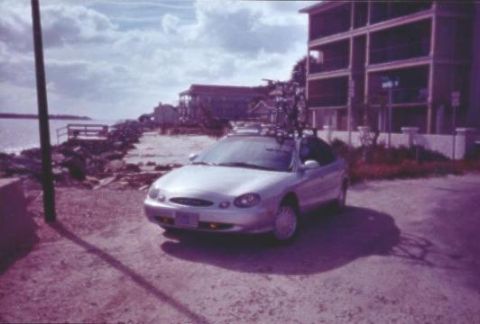 1998 Ford Taurus - A silver 1998 Ford Taurus convertible is parked by the water, with a bike rack on its roof.