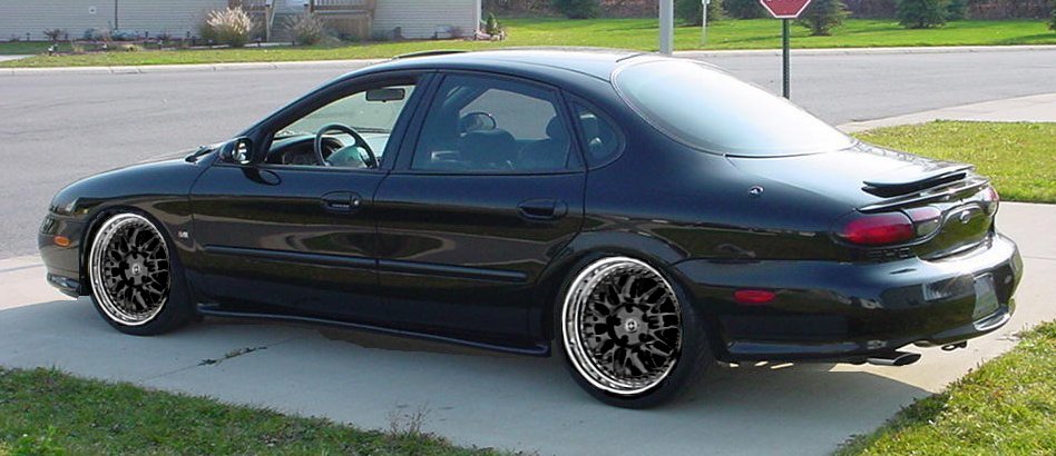 Black Ford Taurus sedan lowered on aftermarket multi-spoke wheels in driveway