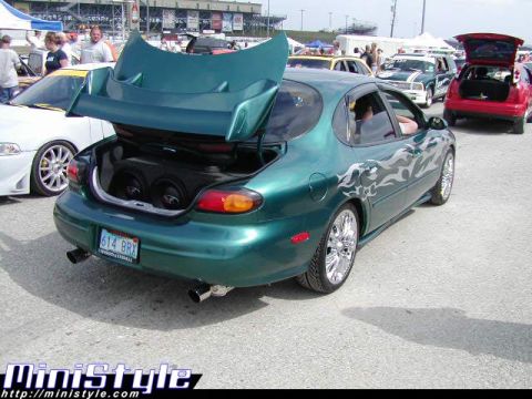 1998 Ford Taurus - Dark teal Ford Taurus sedan at an outdoor car show with its trunk lid raised on a custom lay-back hinge, exposing a pair of subwoofers in a…