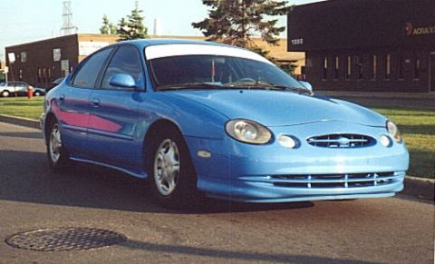 1998 Ford Taurus - Bright blue oval-styled Ford Taurus sedan photographed from the three-quarter front in an office parking lot, with a body-color front air d…