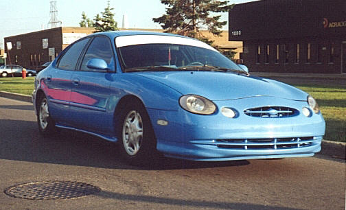Bright blue Ford Taurus sedan with body kit and fog lights in a parking lot