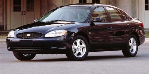 1998 Ford Taurus - A dark navy Ford Taurus sedan photographed in profile-leaning three-quarter front view on pavement in front of a stone building, in the sty…