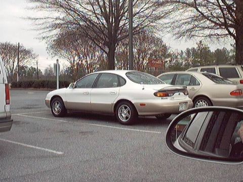 1998 Ford Taurus - A two-tone Ford Taurus sedan, white upper body over a gold lower half with a matching beltline stripe, parked in a bare-tree lot and photog…