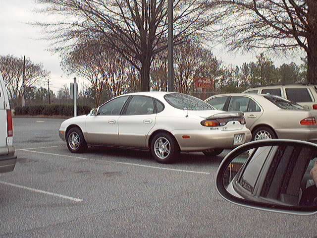 Two-tone white over gold Ford Taurus sedan with decklid spoiler, rear three-quarter view