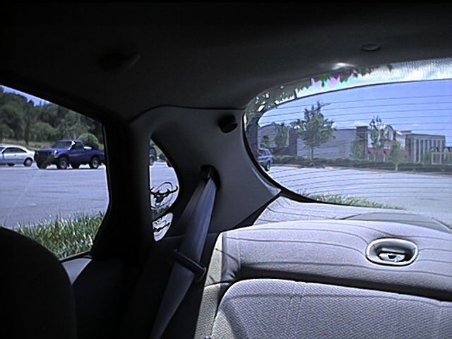 Interior rear quarter showing gray C-pillar, seat belt and window over parking lot