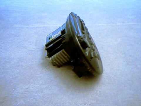 1998 Ford Taurus - Small black electronic module with a finned metal heat sink section and plug-in connector lying on beige carpet; the blurry photo suggests…