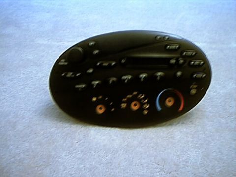 1998 Ford Taurus - An oval black factory Ford radio and climate control head unit removed from the dash and lying face-up on light gray carpet. The face carri…