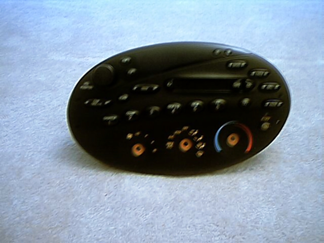 Oval black Ford factory radio and climate control head unit removed and lying on gray carpet